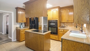 A kitchen with wooden cabinets, a black refrigerator, a stove, and a sink.