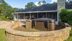 A house with a covered patio area, a hot tub, and a brick fire pit.