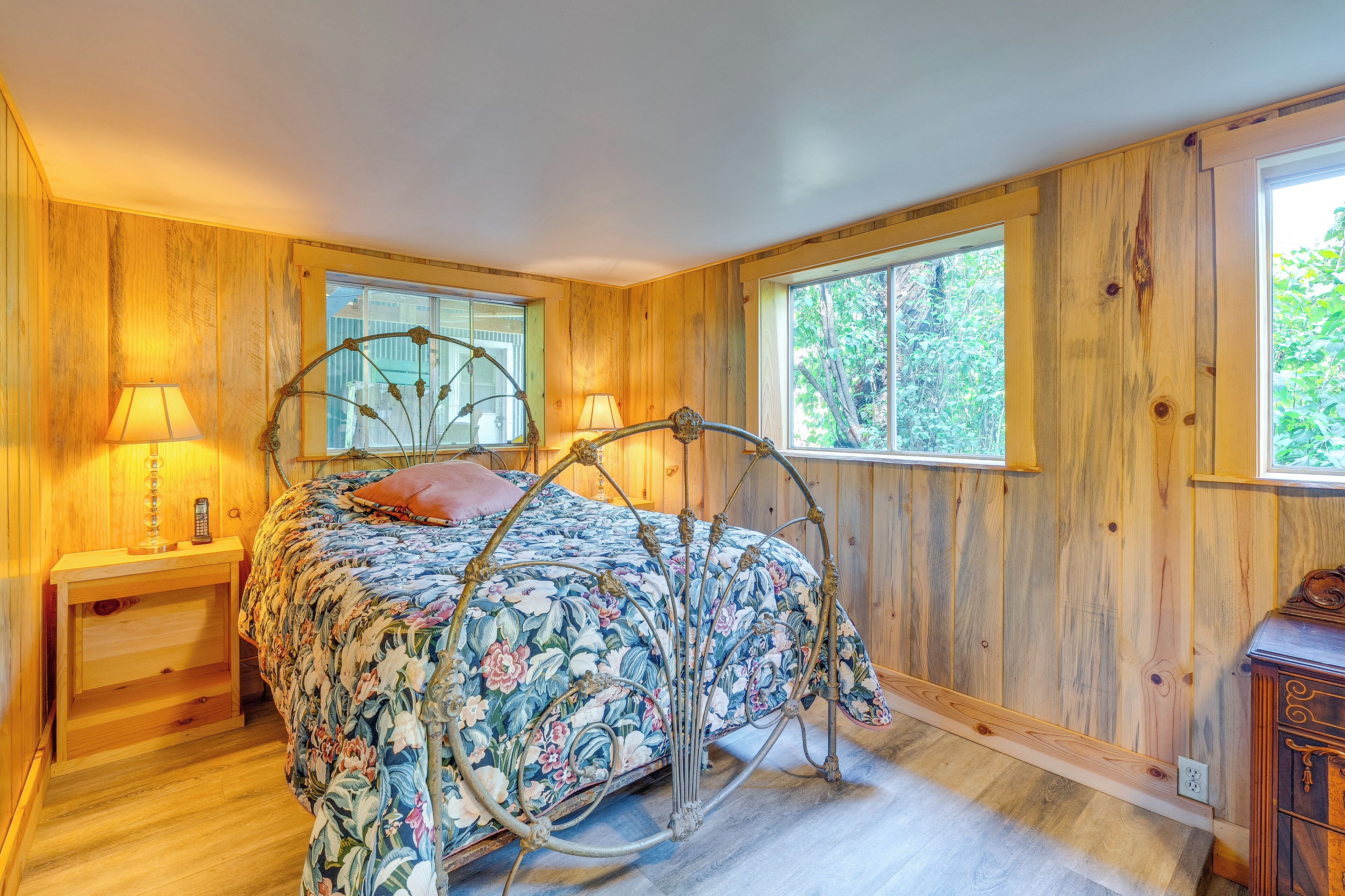 A bedroom with a metal bed frame, wooden walls, and large windows.