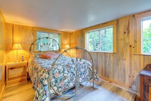 Um quarto com estrutura de cama de metal, paredes de madeira e janelas amplas.