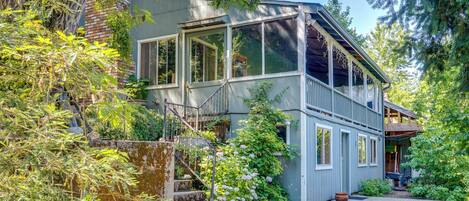 A two-story house with a balcony, surrounded by dense greenery and trees.