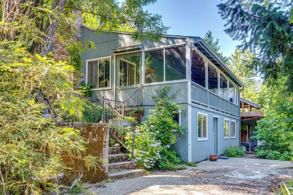 A two-story house with a balcony, surrounded by dense greenery and trees.