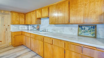 A kitchen with wooden cabinets, a white countertop, a microwave, and a painting on the wall.