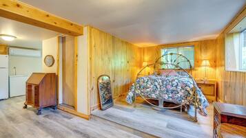 Um quarto com chão de madeira, uma cama com colcha floral, cômoda e janela com vista.