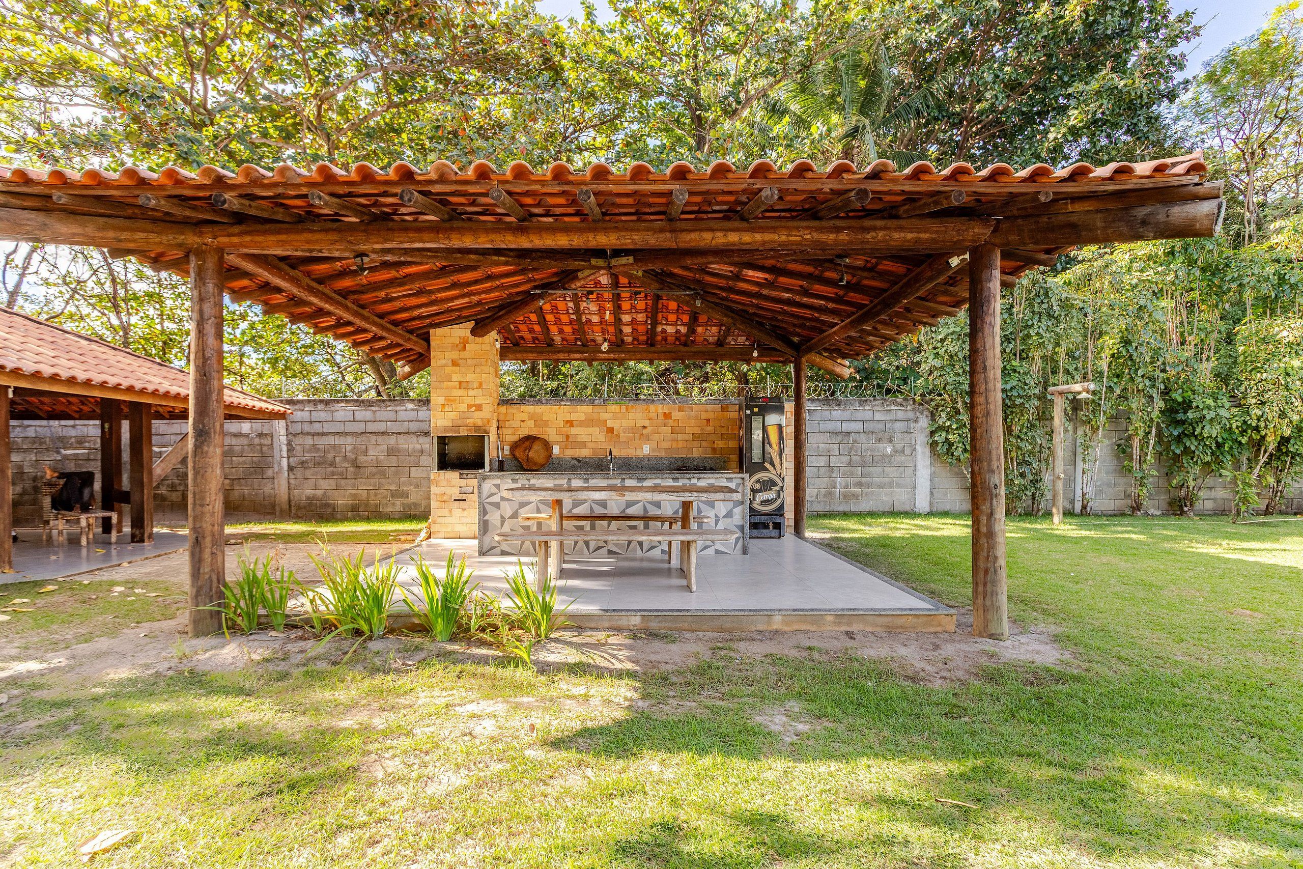 Un área de barbacoa al aire libre con horno de ladrillo, una mesa de madera y un espacio de estar techado.