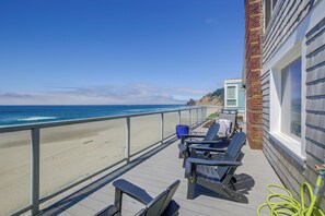 Ein Balkon mit Blick auf Strand und Meer, ausgestattet mit zwei Liegestühlen und einer blauen Mülltonne.