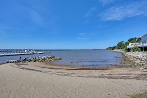 A beach with a rocky shoreline, a pier extending into the water, and a building with a balcony overlooking the beach.