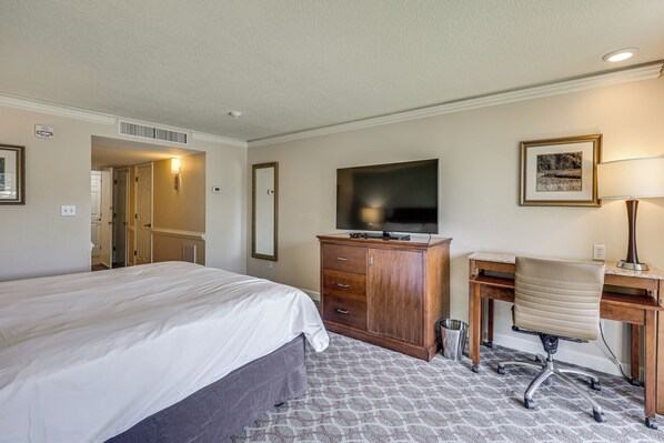A hotel room with a bed, a desk, a chair, a television, and a framed picture on the wall.