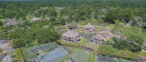 An aerial view of a residential area with multiple houses, green spaces, and a large sports court.