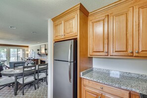A kitchen with wooden cabinets, a stainless steel refrigerator, granite countertop, and a dining area with chairs and a table. - Condo Close to Busch Gardens/colonial Williamsburg (Williamsburg)