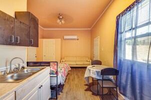 Una habitación compacta con kitchenette, un sofá, una mesita y una silla.