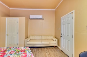 Una habitación con sofá color beige, colcha estampada y equipo de aire acondicionado en la pared.