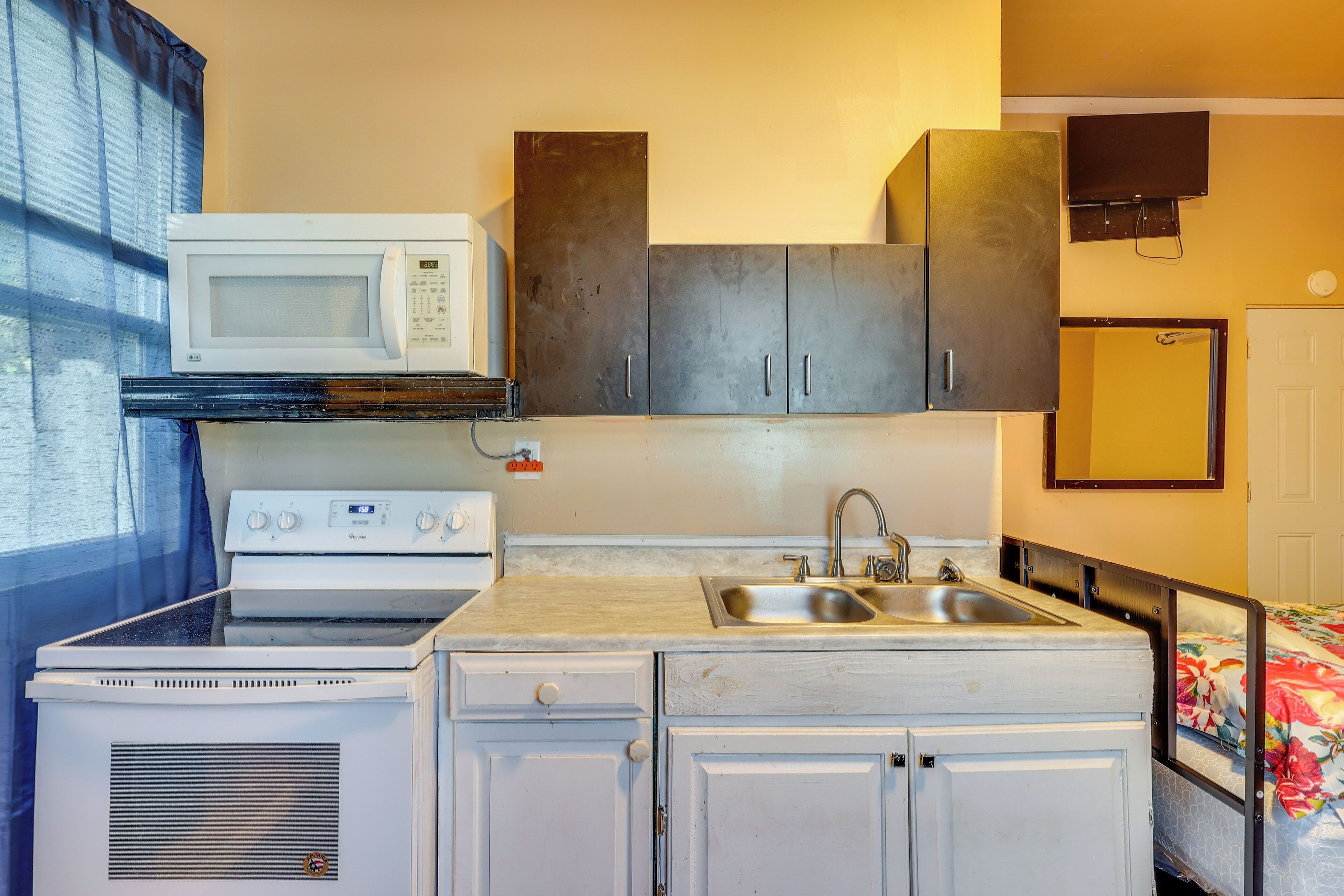 A compact kitchenette with a microwave, stove, sink, and cabinets.