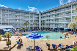 Ein Hotel mit großzügigem Poolbereich, mehreren Balkonen und Liegestühlen.
