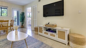 A living room with a flat-screen TV mounted on the wall, a white entertainment unit with electronic devices, a dining area with wooden furniture, and a large potted plant. - Relax, Recharge, Repeat: Hilton Head Resort Condo (Hilton Head Island)