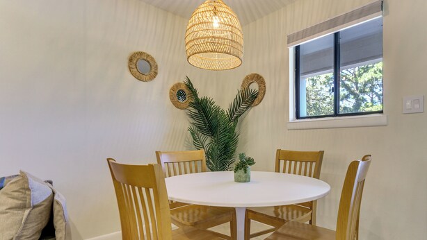 A dining area with a round table, four wooden chairs, a woven light fixture, and wall decor. - Relax, Recharge, Repeat: Hilton Head Resort Condo (Hilton Head Island)