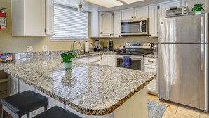 Cocina con encimeras de granito, electrodomésticos de acero inoxidable y armarios blancos.