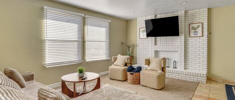 A living room with a fireplace, two sofas, a coffee table, and a flat-screen TV mounted on the wall.