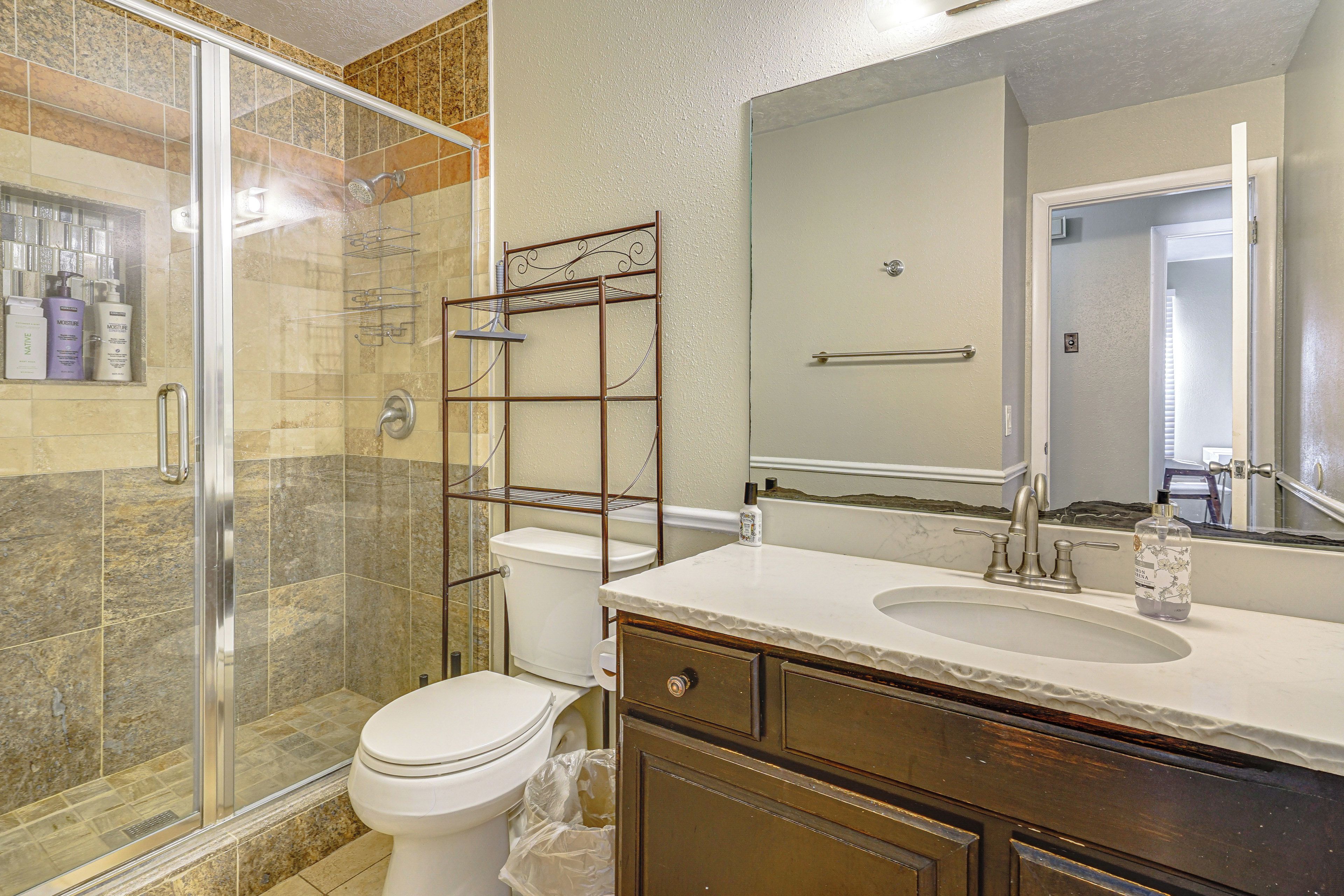A bathroom with a glass shower enclosure, a toilet, a vanity with a sink, and a mirror.