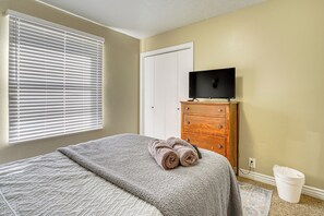 A bedroom with a bed, a dresser, a television on top, and a window with blinds. - Centrally Located Escape in Midvale w/ Yard! (Midvale)