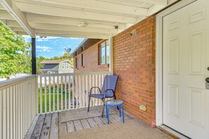 A covered porch with a white railing, a blue chair, and a small table.