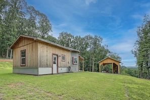 A wooden cabin with a porch and a smaller shed, surrounded by a grassy area and trees. - Outdoor Oasis w/ Mtn Views! 5-acre Augusta Getaway (Augusta)