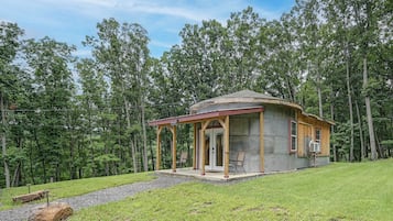A small, single-story cabin with a porch, surrounded by a forest.