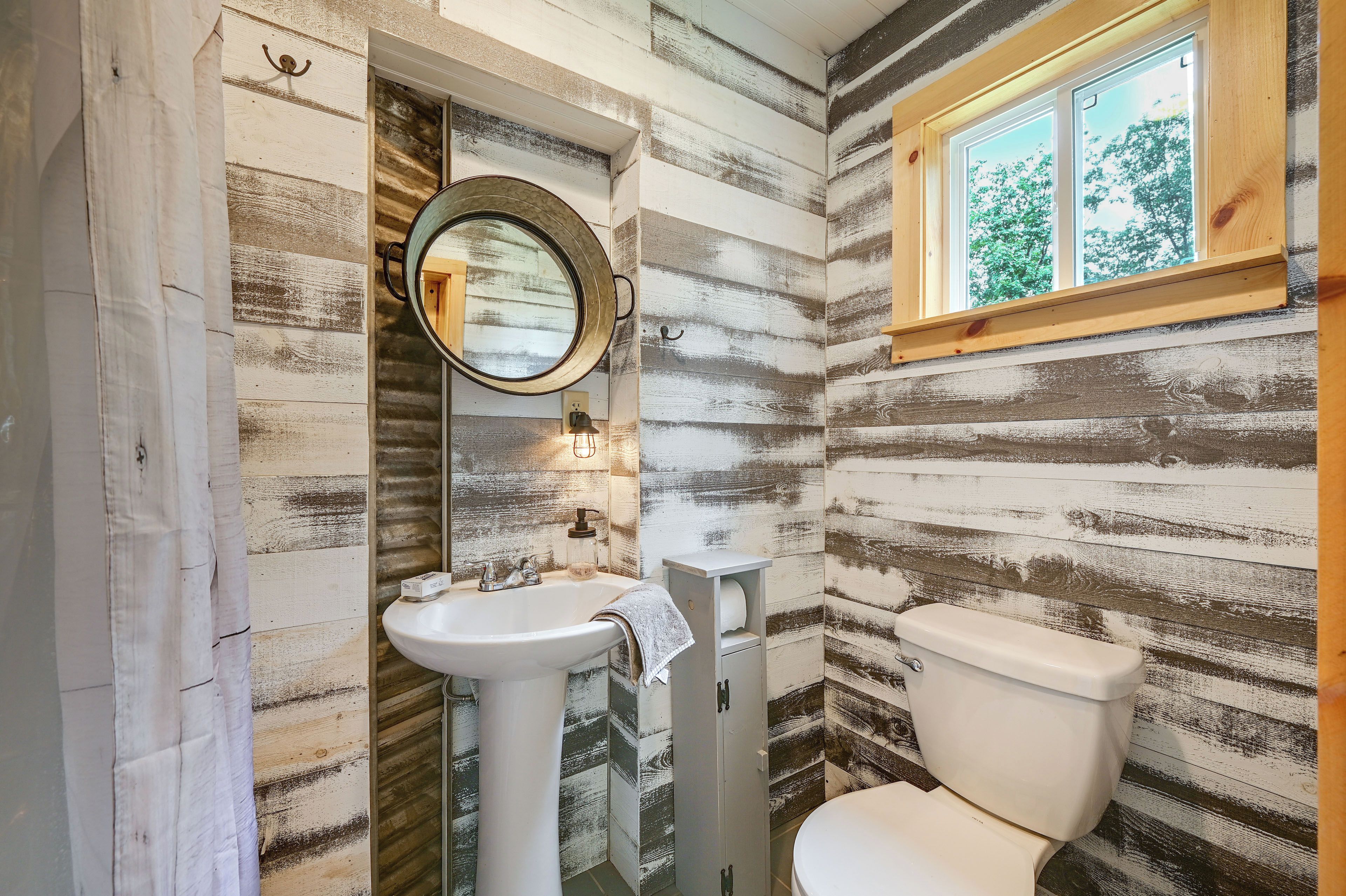 A bathroom with a rustic wooden wall design, a round mirror, a sink, and a toilet.