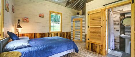 A bedroom with a bed, a window, a fan, and a bathroom with a sink.