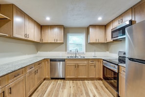 A modern kitchen with wooden cabinets, stainless steel appliances, and a granite countertop.