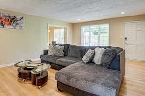A living room with a sectional sofa, a glass coffee table, and hardwood flooring.