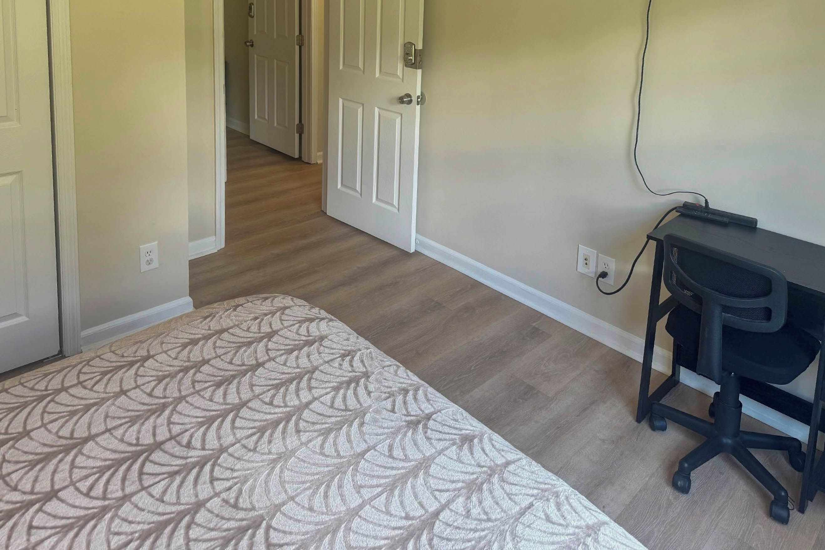 Une chambre à coucher avec une couvre-lit à motifs, un bureau avec une chaise et un couloir menant à une autre pièce.