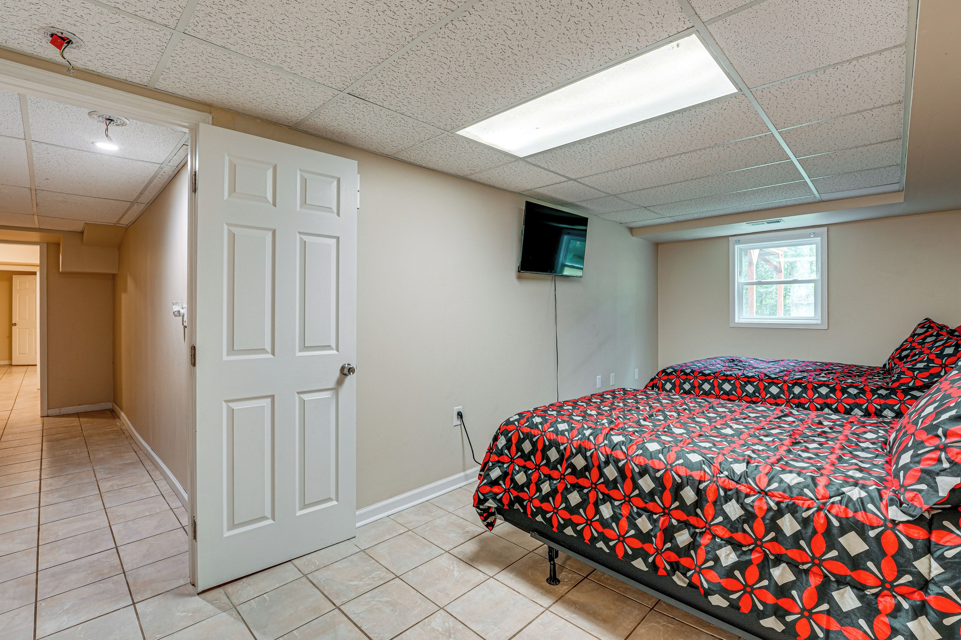 A bedroom with a bed, a door, a television on the wall, and a window.