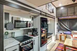 A compact kitchen with a stove, oven, microwave, and a small dining area with a table and chairs. - Hot Tub & Mtn Views! Carlsbad RV Retreat (Carlsbad)