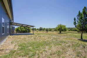 A building with a covered outdoor area, a grassy field, and trees. - Countryside Home Right Outside Fort Worth (Joshua)