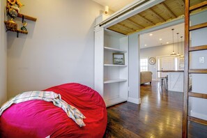 A room with a red bean bag chair, white shelving, a kitchen area, and a wooden ceiling.