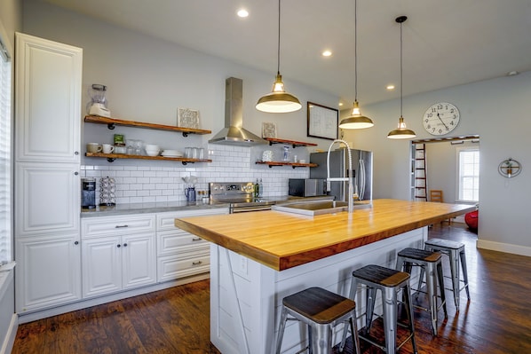 A modern kitchen with white cabinetry, a wooden island, stainless steel appliances, and pendant lighting.