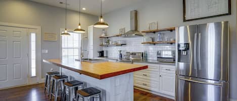 Una cocina moderna con una isla central, electrodomésticos de acero inoxidable, iluminación colgante y vistas al exterior.
