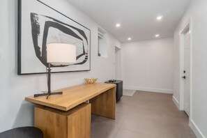 A hallway with a wooden desk, a lamp, and a framed abstract painting on the wall. - Beautiful & Stylish Basement Suite in North Van! (North Vancouver)