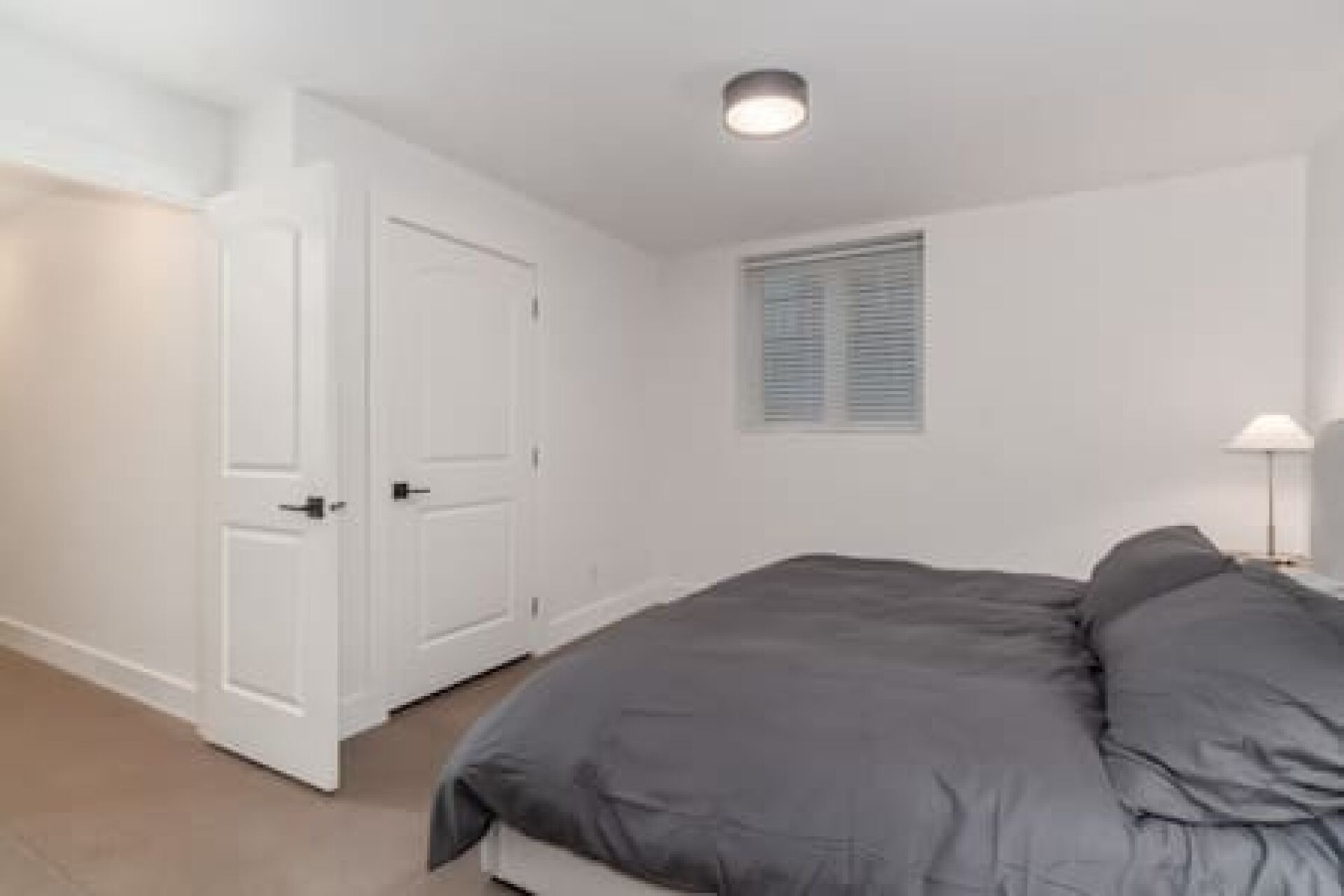 Un dormitorio con una cama, una puerta, una ventana con persianas y una lámpara.