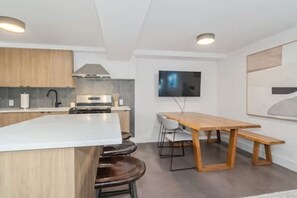 A modern kitchen with a central island, a dining table with chairs, and a flat-screen TV mounted on the wall. - Beautiful & Stylish Basement Suite in North Van! (North Vancouver)