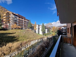 Un quartier résidentiel avec des immeubles à plusieurs étages, un ruisseau et des montagnes en arrière-plan.