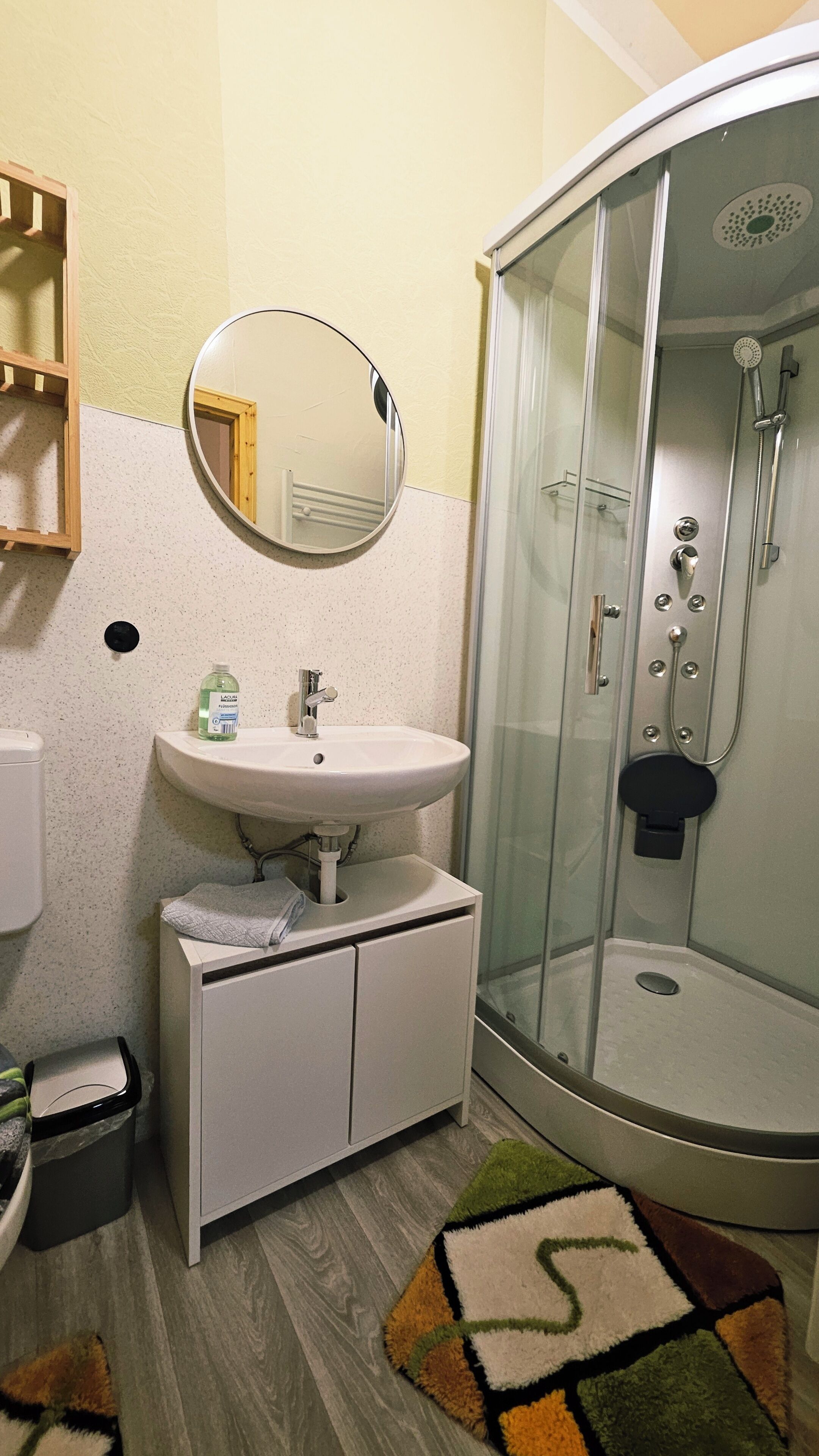 Ein Badezimmer mit Waschbecken, einem Spiegel, einer Duschkabine aus Glas und einem kleinen Teppich.