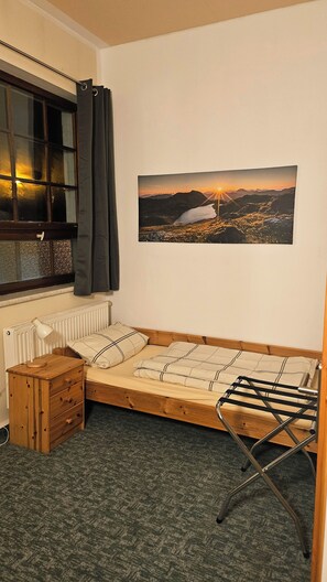 A small, cozy room with a single bed, a wooden nightstand, a radiator, and a window with curtains. - Burgblick  (Nossen)