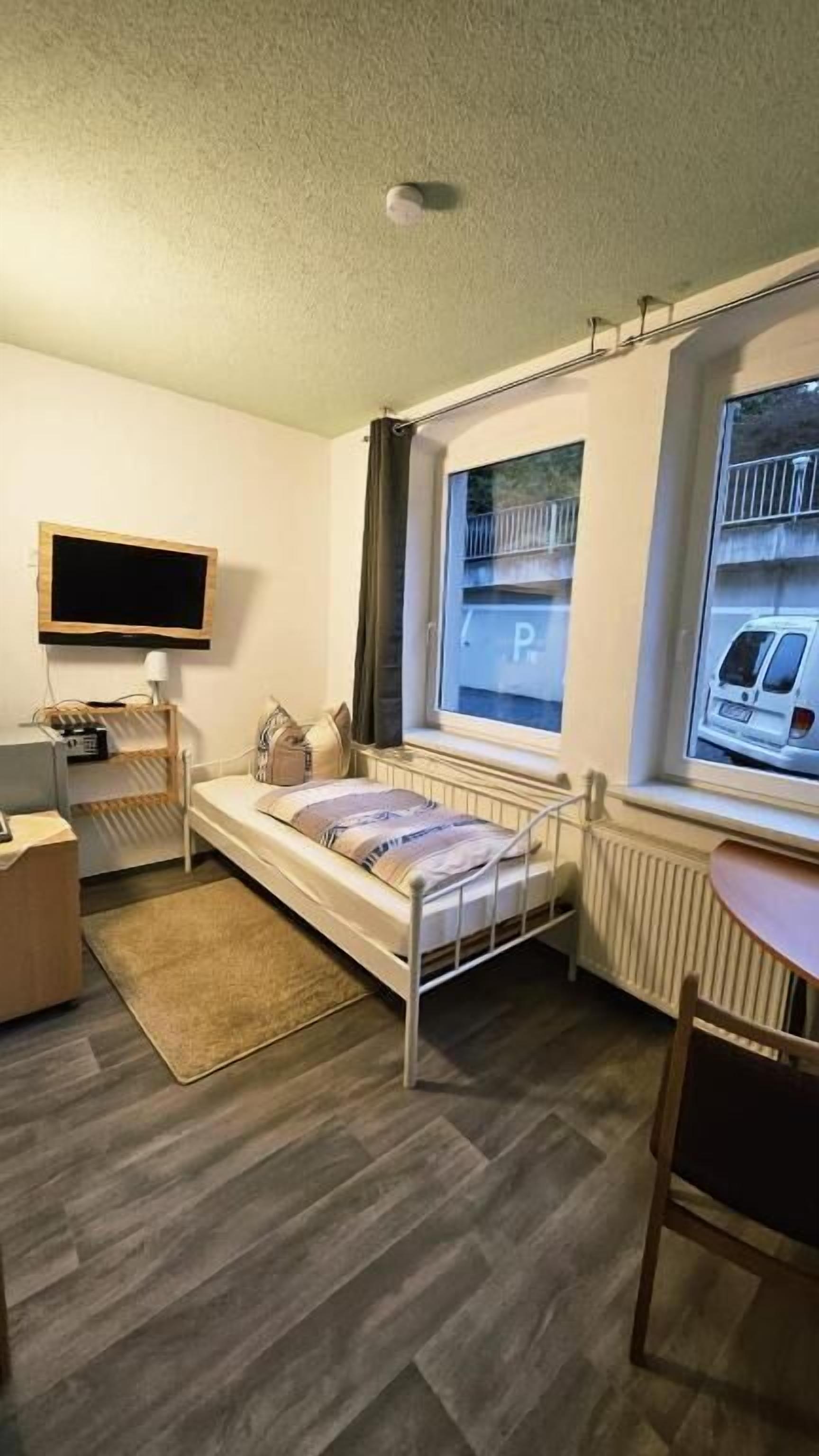 A compact room with a single bed, a desk, a chair, and a television mounted on the wall.