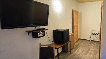 Une pièce avec un téléviseur à écran plat fixé au mur, une petite table avec une chaise, un meuble en bois et une porte au fond.