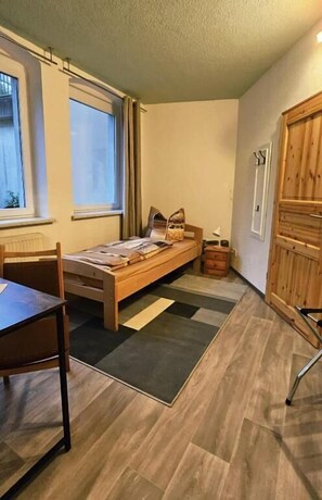 A room with a bed, a chair, a table, a window, and a wardrobe.