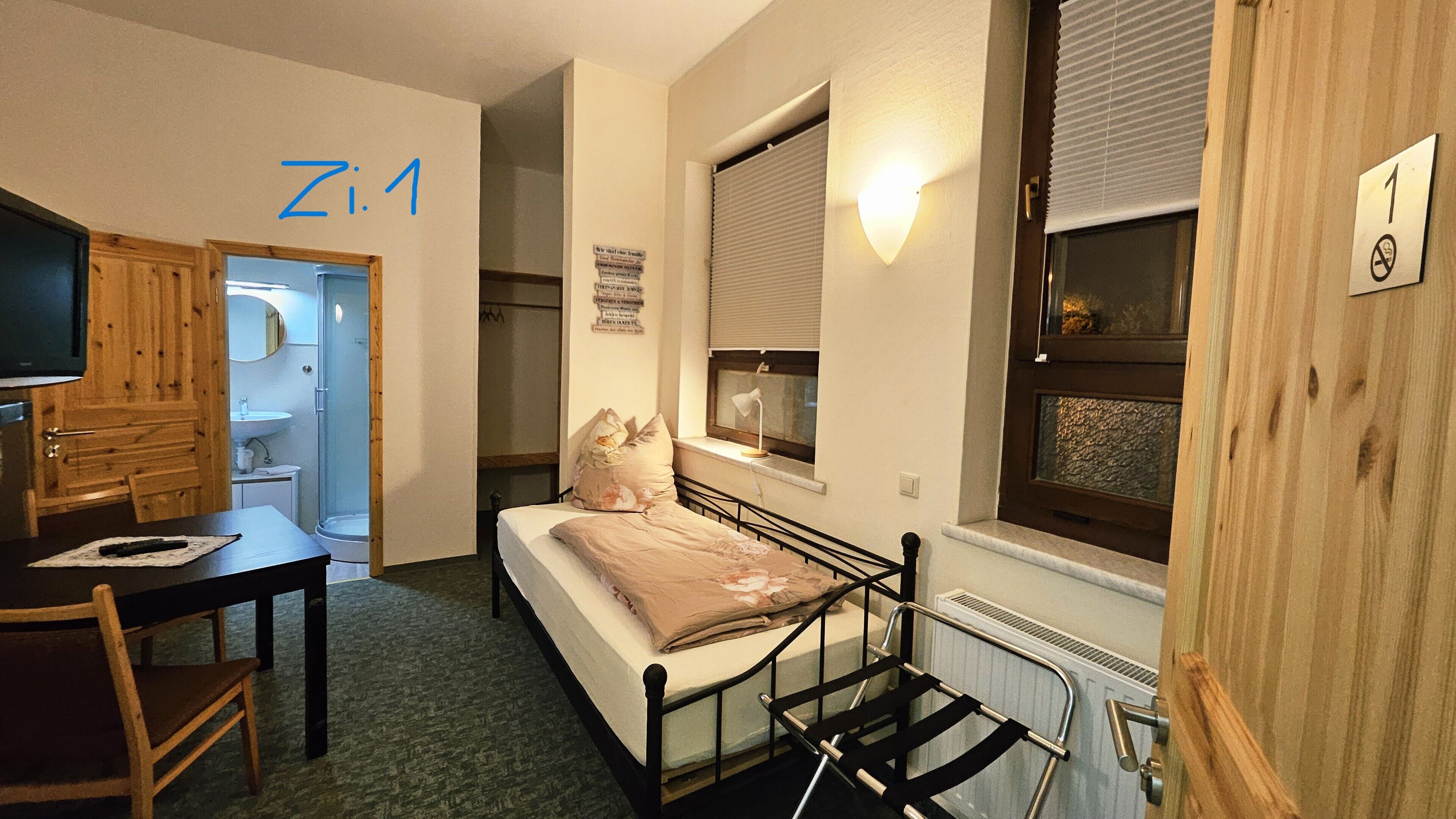 A compact room with a bed, a desk, a chair, a window with blinds, and a radiator.
