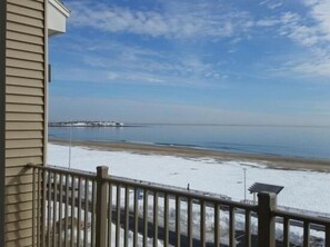 Ein Küsteneigentum mit Balkon und Meerblick, ein Steg in der Ferne sowie ein Sandstrand.
