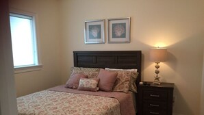 Ein Schlafzimmer mit einem Bett, einem Nachttisch, einer Lampe und zwei gerahmten Bildern an der Wand.
